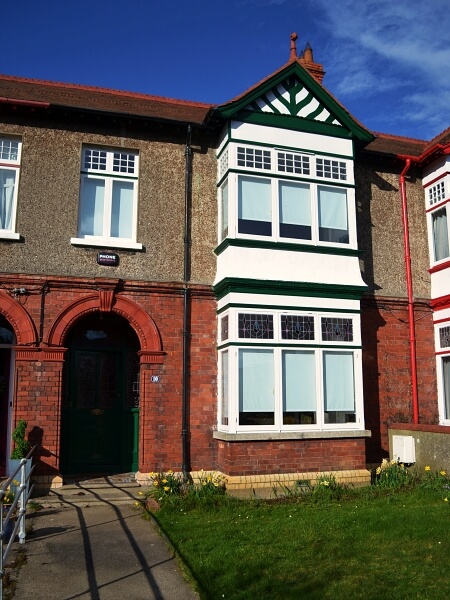 Photograph of a Dublin period home with a pebble dash facade on the first floor and red brick on the ground floor. New white double glazed casement bay windows with granite windows sills. Green front door and grass on the front