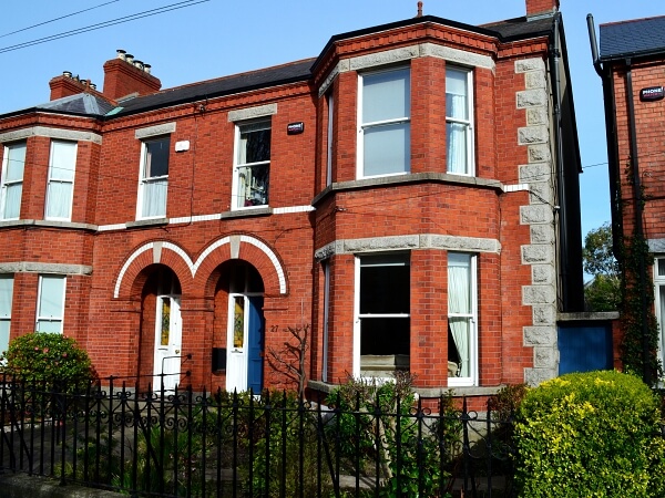 Exterior photograph of a period red brick facade home with white bay sash window, blue period front door, granite steps and window sills.