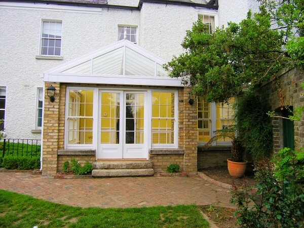 Exterior photograph of a period home featuring a sun room with period white panelled sash windows and panelled french doors.