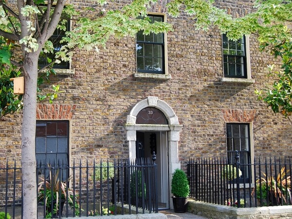 Photograph of the front of a period property with a brick facade and back panelled sash windows with a matching back period front door.