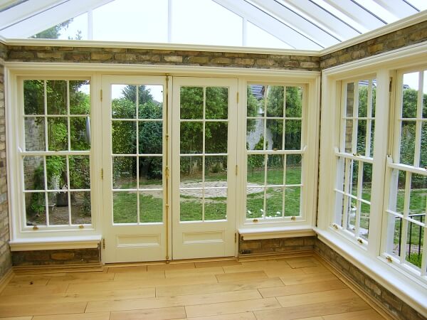 Exterior photograph of interior of a sunroom with period white panelled sash windows and panelled french doors.