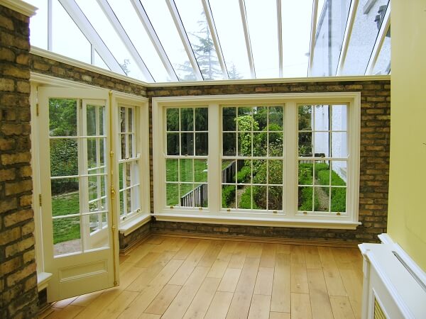 Exterior photograph of interior of a sunroom with period white panelled sash windows and panelled french doors.