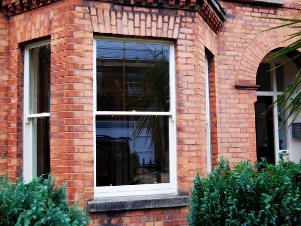Close-up exterior photograph of a period red brick facade home with white sash bay window and granite window sills.