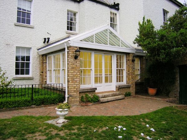 Exterior photograph of a period home featuring a sun room with period white panelled sash windows and panelled french doors.