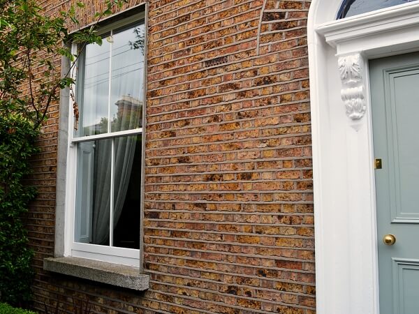 Close-up exterior photograph of a period brick facade home with white panelled sash window and granite window sills.