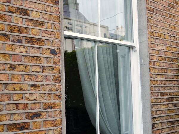 Close-up exterior photograph of a period brick facade home with white panelled sash window and granite window sills.