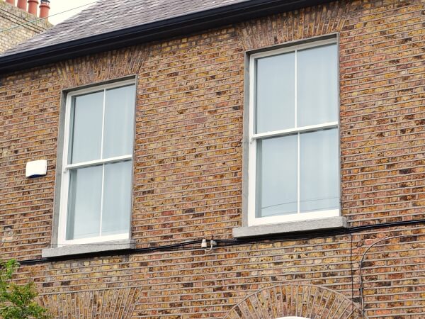 Close-up exterior photograph of a period brick facade home with white panelled sash window and granite window sills.