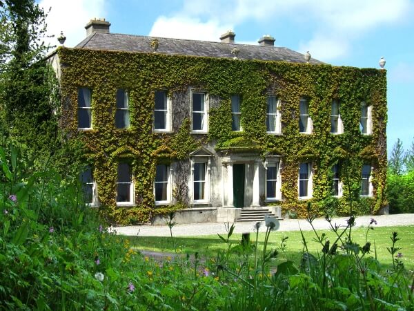 Photograph of the front of Cabinteely House a period property covered in beautiful ivy, featuring multiple white sash windows and front porch.