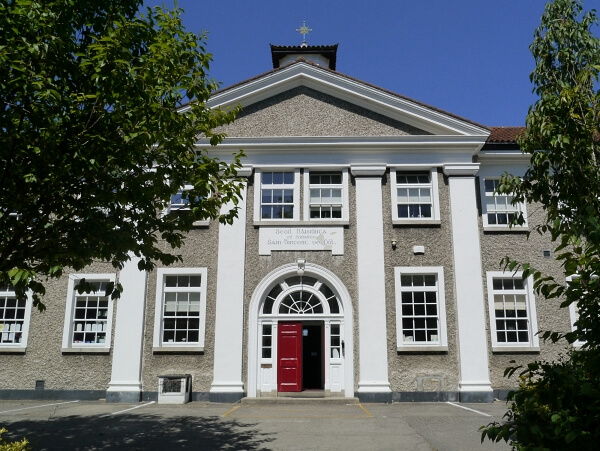 Grey pebble-dash 2 storey building with a dark red double door, a fan arch above it, white pillars and restored sash windows by Bolger Sash Windows on both levels