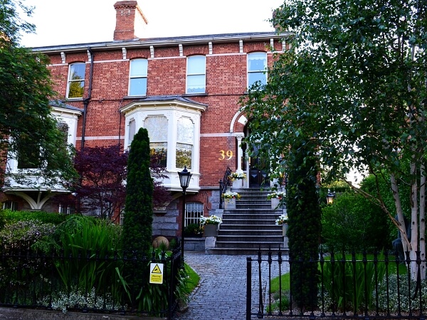 Exterior photograph of a period red brick facade home with white bay sash window, black period front door, granite steps and window sills.