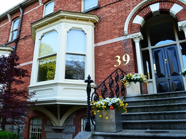 Exterior photograph of a period red brick facade home with white bay sash window, black period front door, granite steps and window sills.
