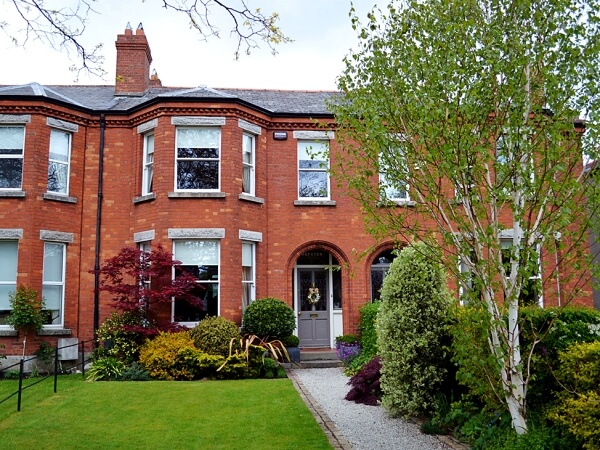 Exterior photograph of a period red brick facade home with white sash window, period front door, granite steps and window sills.
