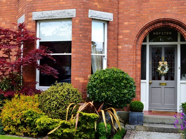 Close-up exterior photograph of a period red brick facade home with white sash window, period front door, granite steps and window sills.