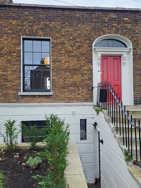 Close up of a Georgian house with brown brick on the upper level and painted white blocks on the lower level. Steps up to a red door on the right. New sash windows painted black on the top and bottom floors on the left