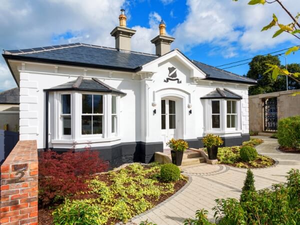Photograph of the beautiful period gate lodge "Knockrabo" featuring white penelled sash windows and landscapes front garden.